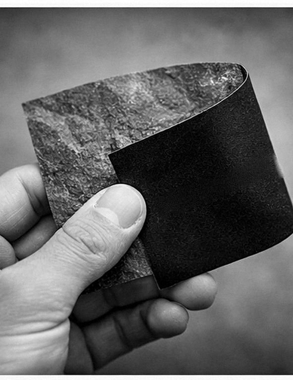 A hand flexes a Flexistone swatch between thumb and forefinger, showing the split-stone face and the plain backing, black and white
